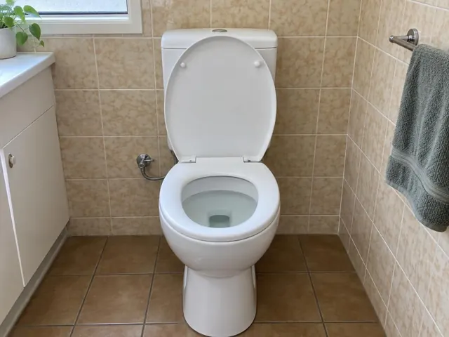 Clean white toilet in a beige tiled bathroom with tiled floor and towel rail in The Ponds