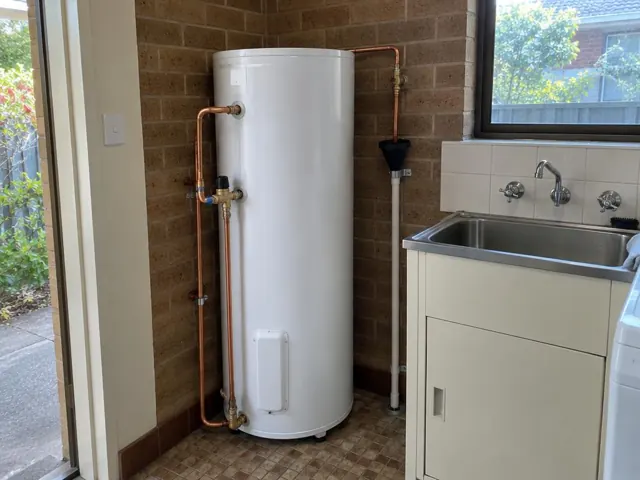Indoor hot water cylinder beside a laundry sink with copper pipework and tiled walls in Box Hill